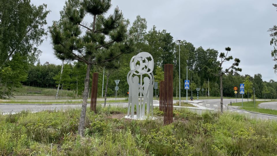 En plåtsvetsad skulptur föreställande barn som står i en ring och håller varandras händer placerad i mitten av en rondell intill en tall.