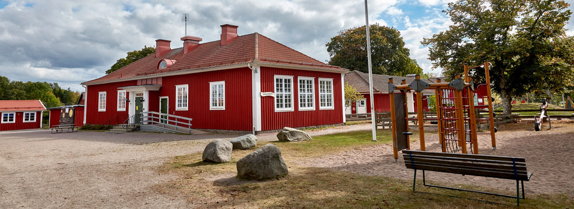 En röd träbyggnad med grön dörr, till vänster om skolan står en klätterställning